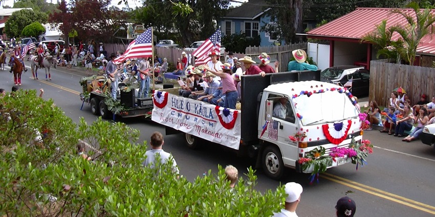 Parade horses and riders in Makawao pass homes decorated with American flags for July 4.