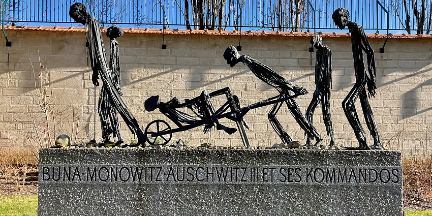 Metal sculpture of emaciated figures pushing a cart, mounted on a stone Holocaust memorial.