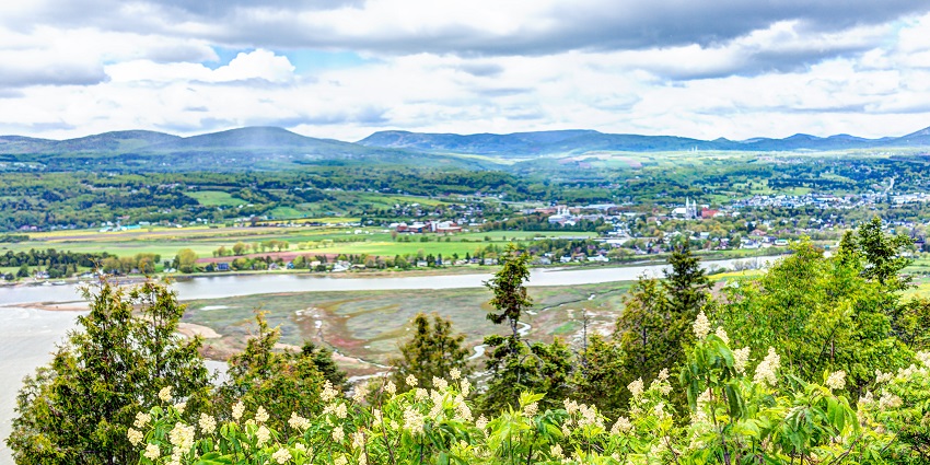 Skyline of Baie-Saint-Paul with buildings, river, and mountains in the background.