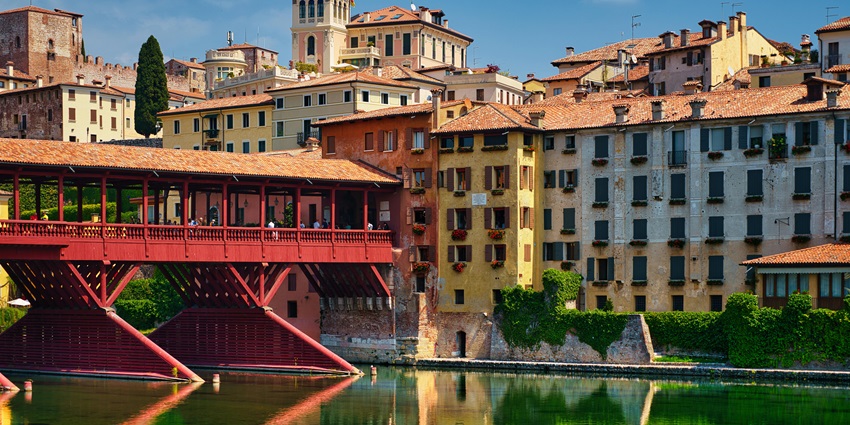 Bassano del Grappa, with a still water body and a red architectural bridge over the river, amongst the best places to visit near Venice.