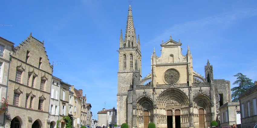 Gothic-style cathedral with a tall spire in a quiet town square under a bright blue sky.