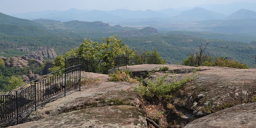 Belogradchik rocks in Bulgaria with black steel railings on the rocks and green mountains.