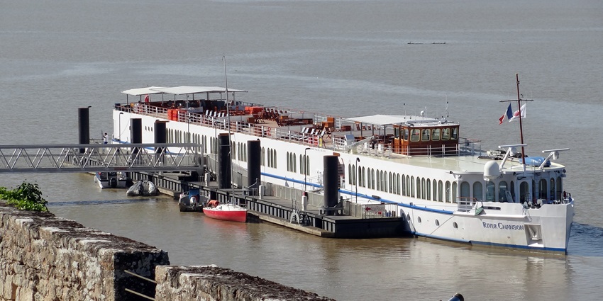 A river cruise ship docked on the calm waters with a stone wall, one of the places to visit near Bordeaux.