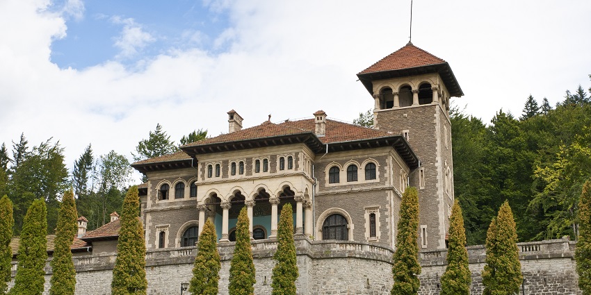 An elaborate neo-Romanian-style mountain fortress surrounded by green trees, one of the best places to visit near Bucharest.