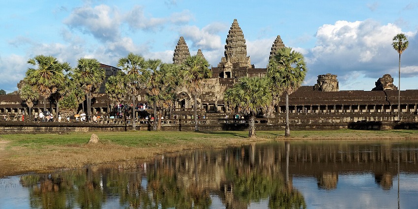 Stunning Angkor Wat at sunrise with reflection and palm trees, one of the top places to visit near Thailand.
