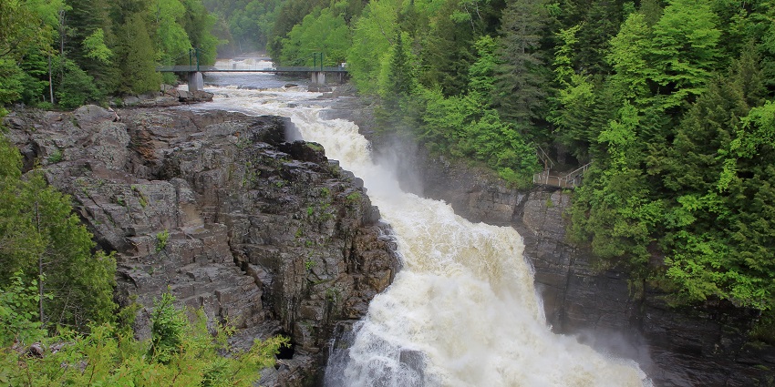 Canyon Sainte Anne with water flowing on a rocky surface and trees on sides, one of the scenic places to visit near Quebec City.
