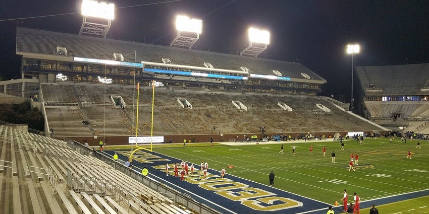 Football players warming up on a lit stadium field at night with mostly empty bleachers.