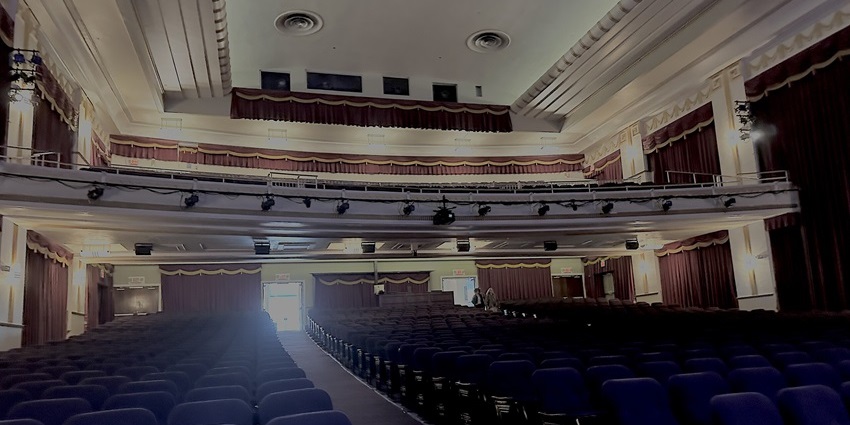 Empty vintage-style theater auditorium with seats, curtains, and upper balcony seating.