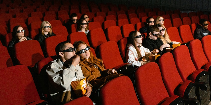 People sitting on the red velvet chairs in a cinema hall while wearing black 3d glasses.