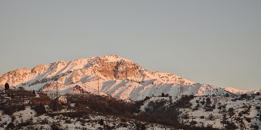Snow-covered Chimgan Mountains with the sun setting and highlighting the scenery.