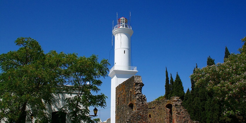 Colonia del Sacramento lighthouse with a white architectural tower and old broken walls nearby.