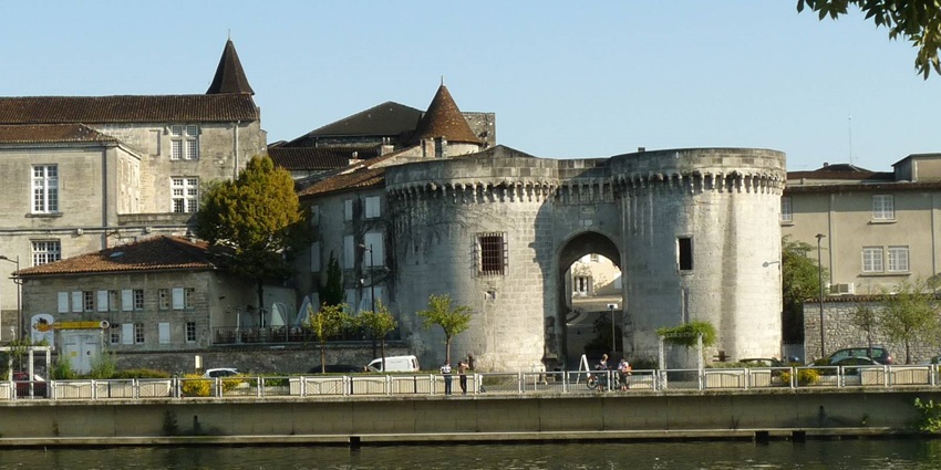 Historic stone gatehouse with twin round towers reflected in a river under blue sky.