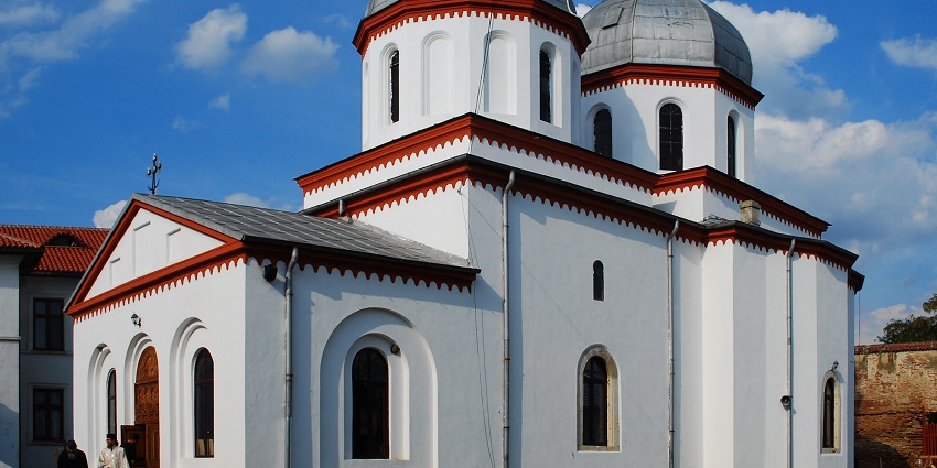 White Orthodox church with red trim and silver domes under a bright sky, one of the places to visit near Bucharest.