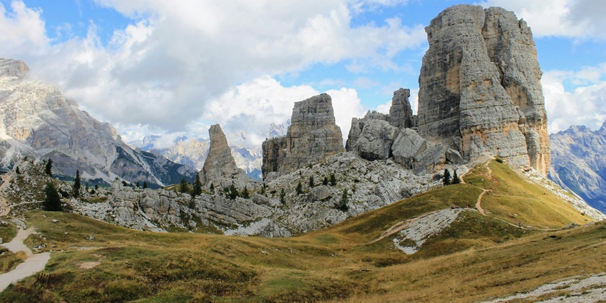 Cortina d’Ampezzo with a unique rock structure, green trees, and snow mountains at a distance.