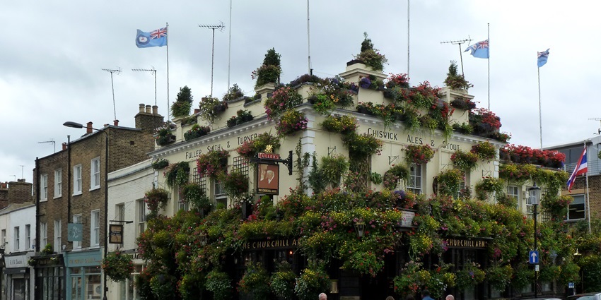 The Churchill Arms pub in London adorned with flowers and multiple national flags on top.