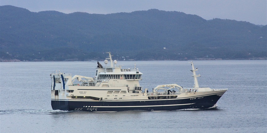 A boat in the calm, clear waters of Kings Bay, with forested hills in the background.

