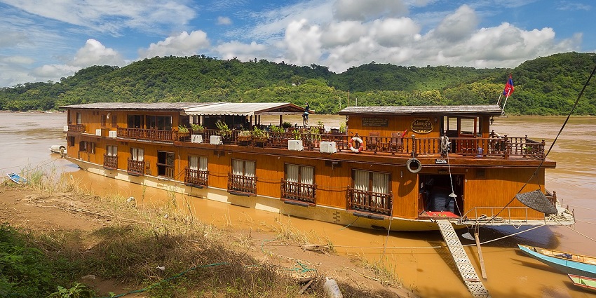 The Mekong Sun cruise docked along the Mekong River near Luang Prabang, with hills behind.