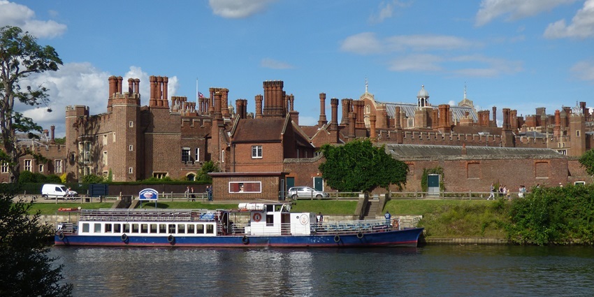 A brick castle with tall chimneys stands behind a docked riverboat, one of the best things to do in Nowitch.