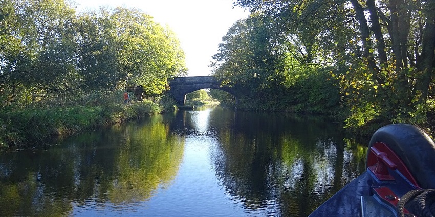 Union Canal with calm water flowing under a stone overbridge, surrounded by greenery.