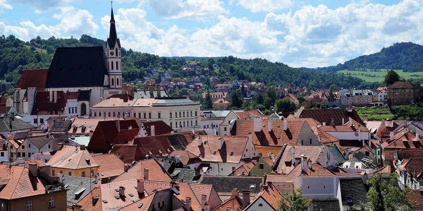 Scenic view of Český Krumlov in the Czech Republic with red rooftops, a church tower, and hills.
