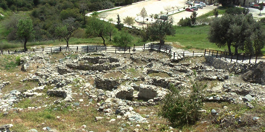 Ancient circular stone dwellings at the Choirokoitia archaeological site with dry grass.