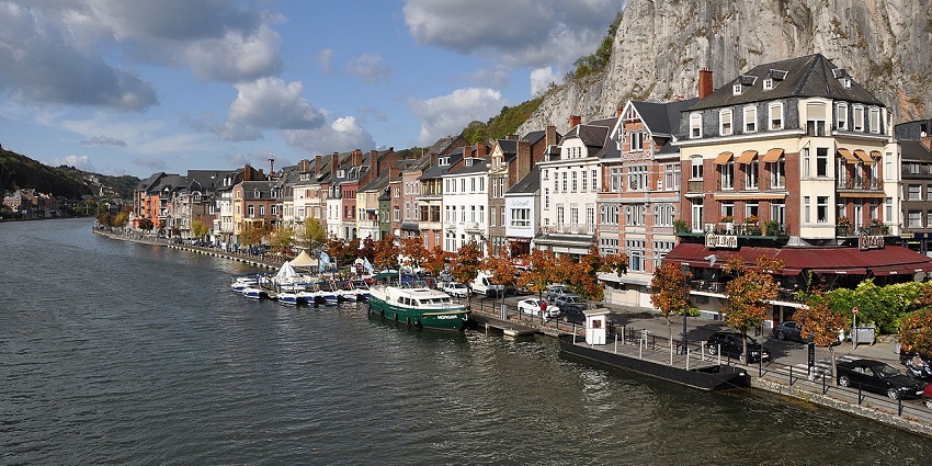 Riverside view of colorful townhouses, boats, and cliffs, amongst the top places to visit near Brussels.