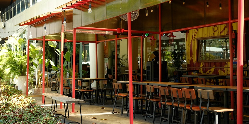 Outdoor seating area of a café with unique chairs, tables, greenery, and a large window.