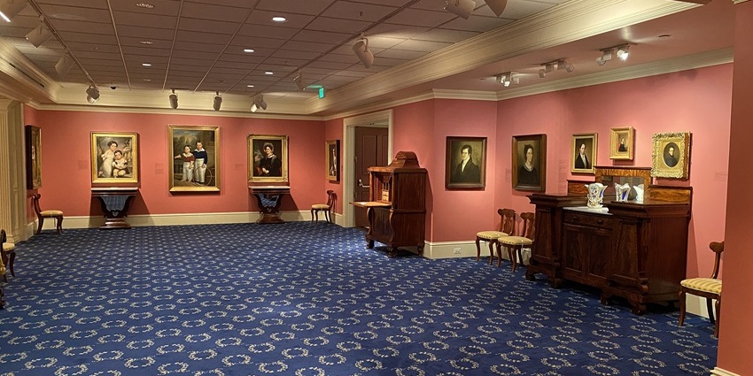 Elegant gallery room with patterned carpet, classic portraits, and antique furniture.