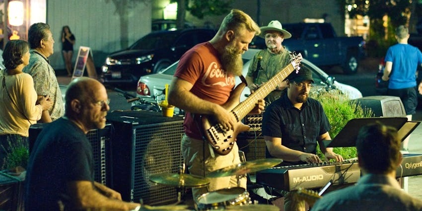 A musician playing a guitar during a live music performance in an outdoor setting.