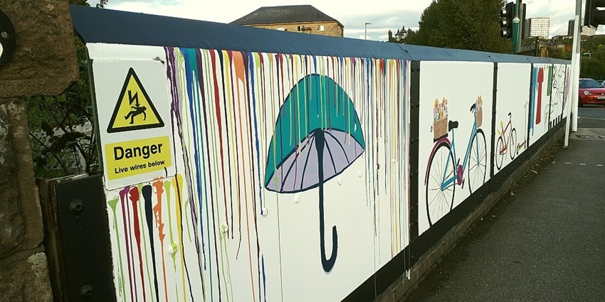 Art panel on the wall of Kirkstall railway bridge featuring figures and abstract patterns.