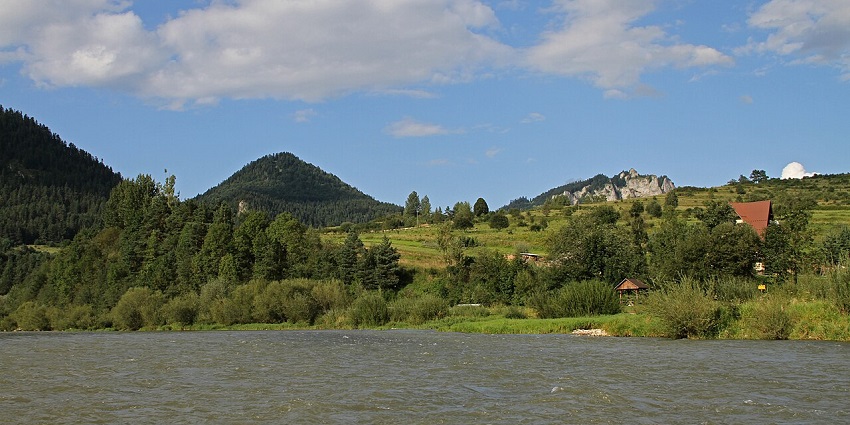 A scenic river winds through lush green hills and rugged mountain peaks under a clear blue sky.