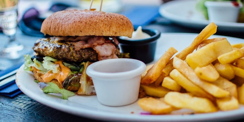 Burger with vibrant vegetables & sauces in the burger, French fries served on a white plate.