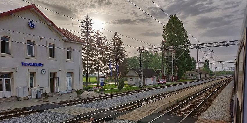 A quiet train station at sunrise with empty tracks, a station building, and cloudy skies.