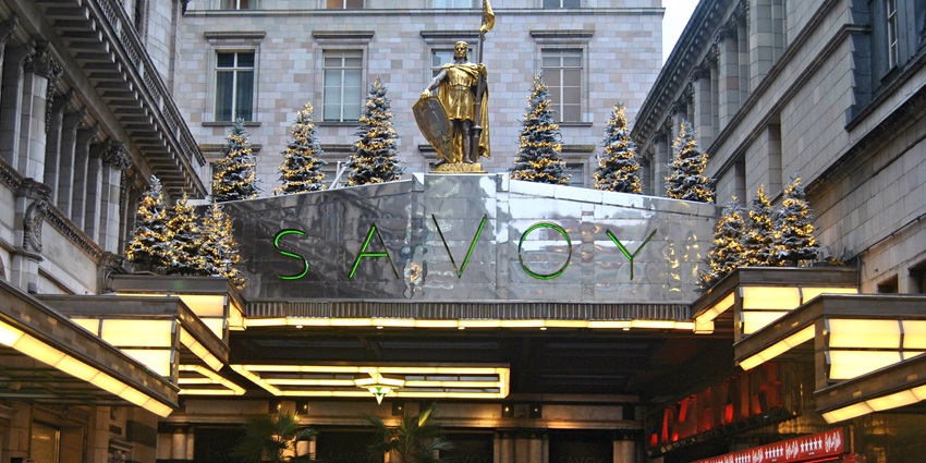 The Savoy Hotel entrance is adorned with Christmas lights and small decorated trees outside.