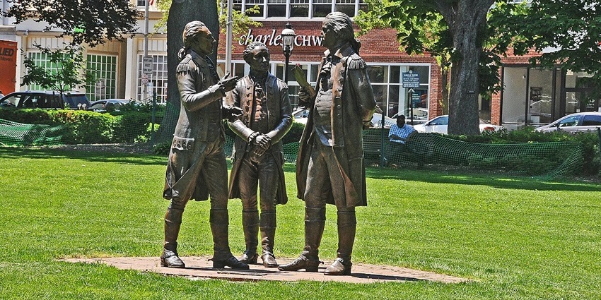 Bronze statues of three men in colonial attire standing together on a green lawn.