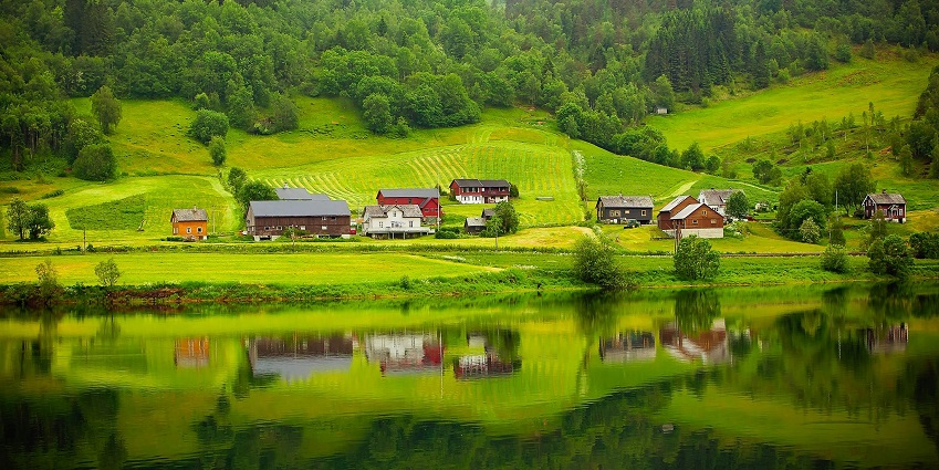 Valley farm with distant farm buildings & houses, a river in the front and green trees.