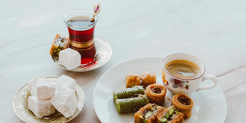 Baklava with coffee, blocks of sugar, and tea served on white plates and designer cups.