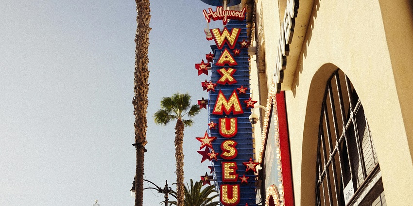 Hollywood Wax Museum sign with bright lights and palm trees on a sunny street corner.
