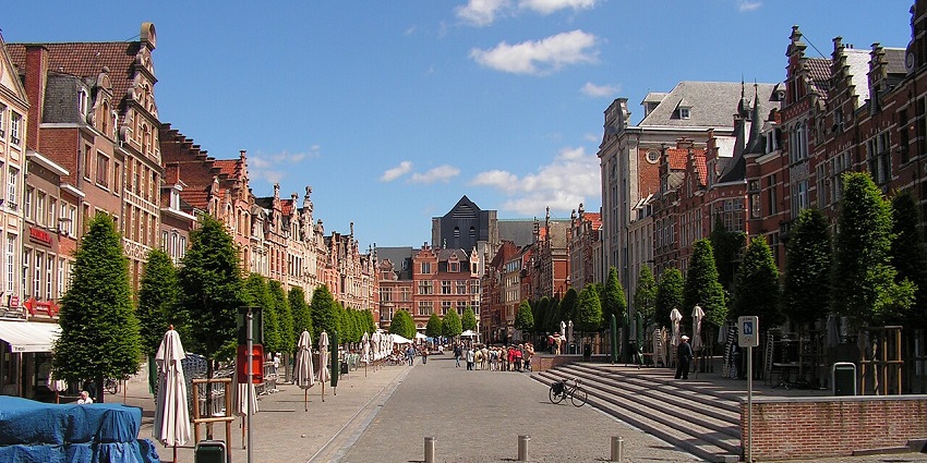 Oude Markt square in Leuven is framed by tall trees and historic Flemish-style buildings.
