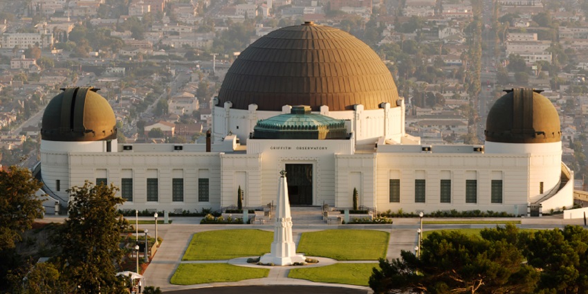 Front view of Griffith Observatory with green lawn and cityscape in the valley behind.