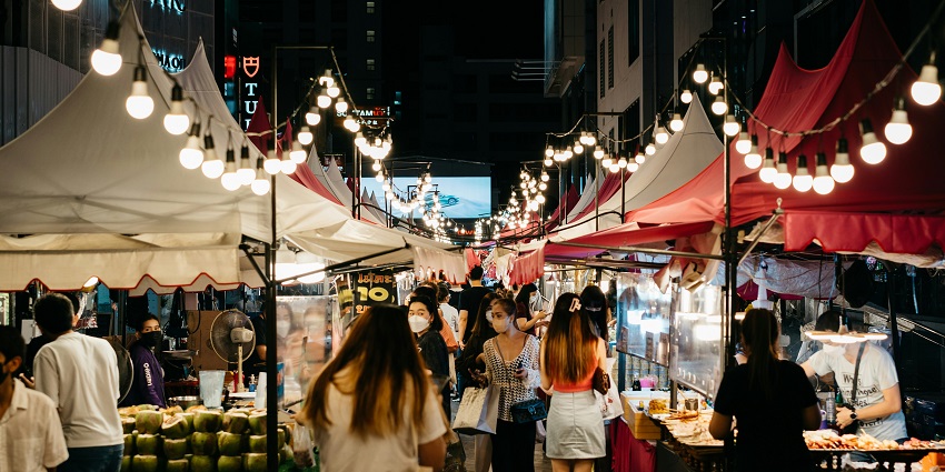 Night market with multiple distant shops & eating places and people visiting the market.

