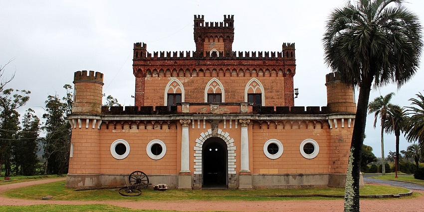 Front facade of Castillo de Piriá in Piriapolis with traditional architecture and cartwheels nearby.
