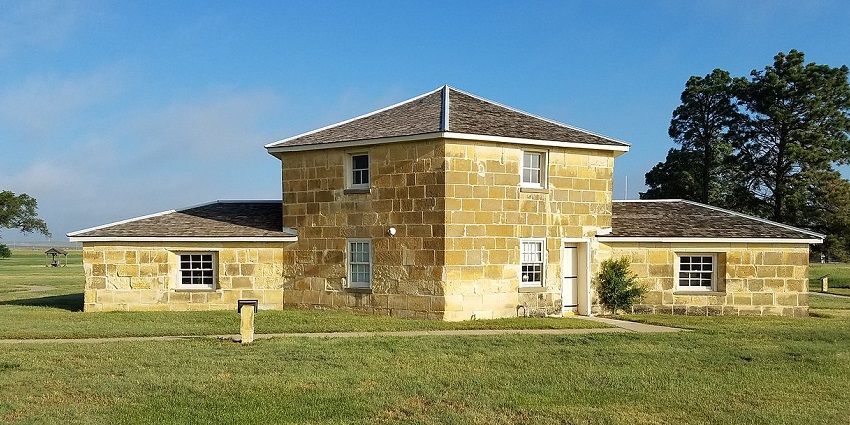 The Iconic stone blockhouse is situated in the Fort Hays historic site, surrounded by trees.