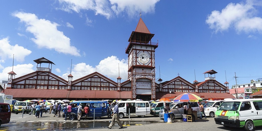 Building of the Starboek market in Georgetown with multiple vehicles parked and people visiting.
