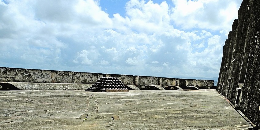 Stacked cannonballs on a stone fort platform under a partly cloudy sky with ocean, one of the best things to see in Old San Juan.