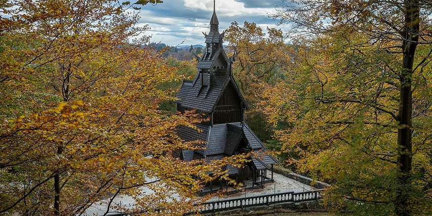 Fantoft Stave Church with black wooden architecture, fence, and tall trees, unique places to visit near Bergen.