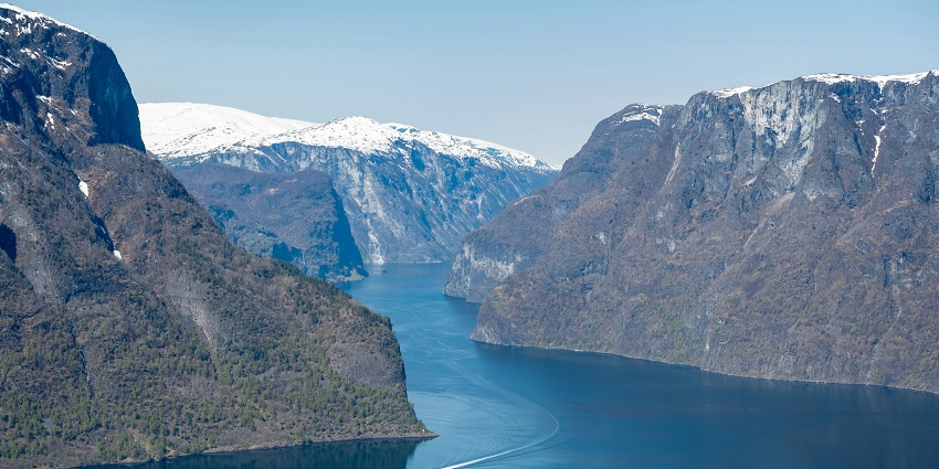 Aerial view of Flåm featuring a calm water body, a boat, and snow-covered mountain peaks.