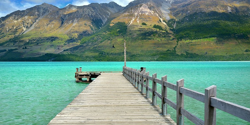 Wooden bridge over still water with mountain backdrop in scenic Glenorchy landscape.