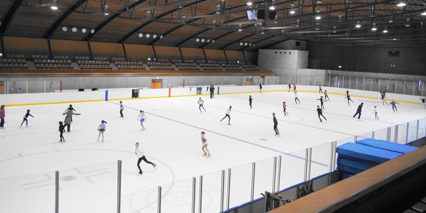 Indoor ice skate park with multiple unique white lightings, people ice skating and seats