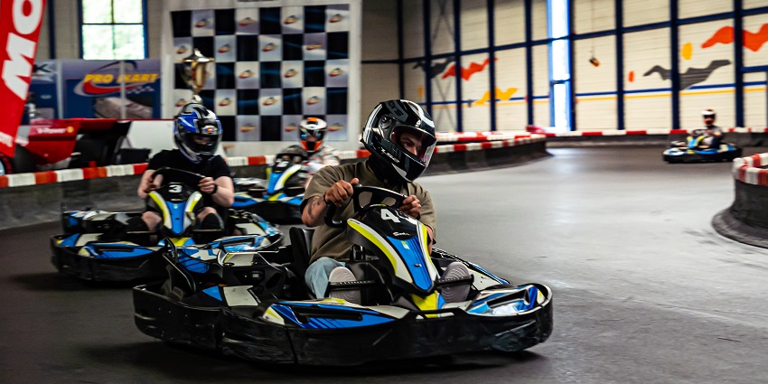 People racing go-karts on an indoor track in Hohenfels, wearing helmets and safety gear.